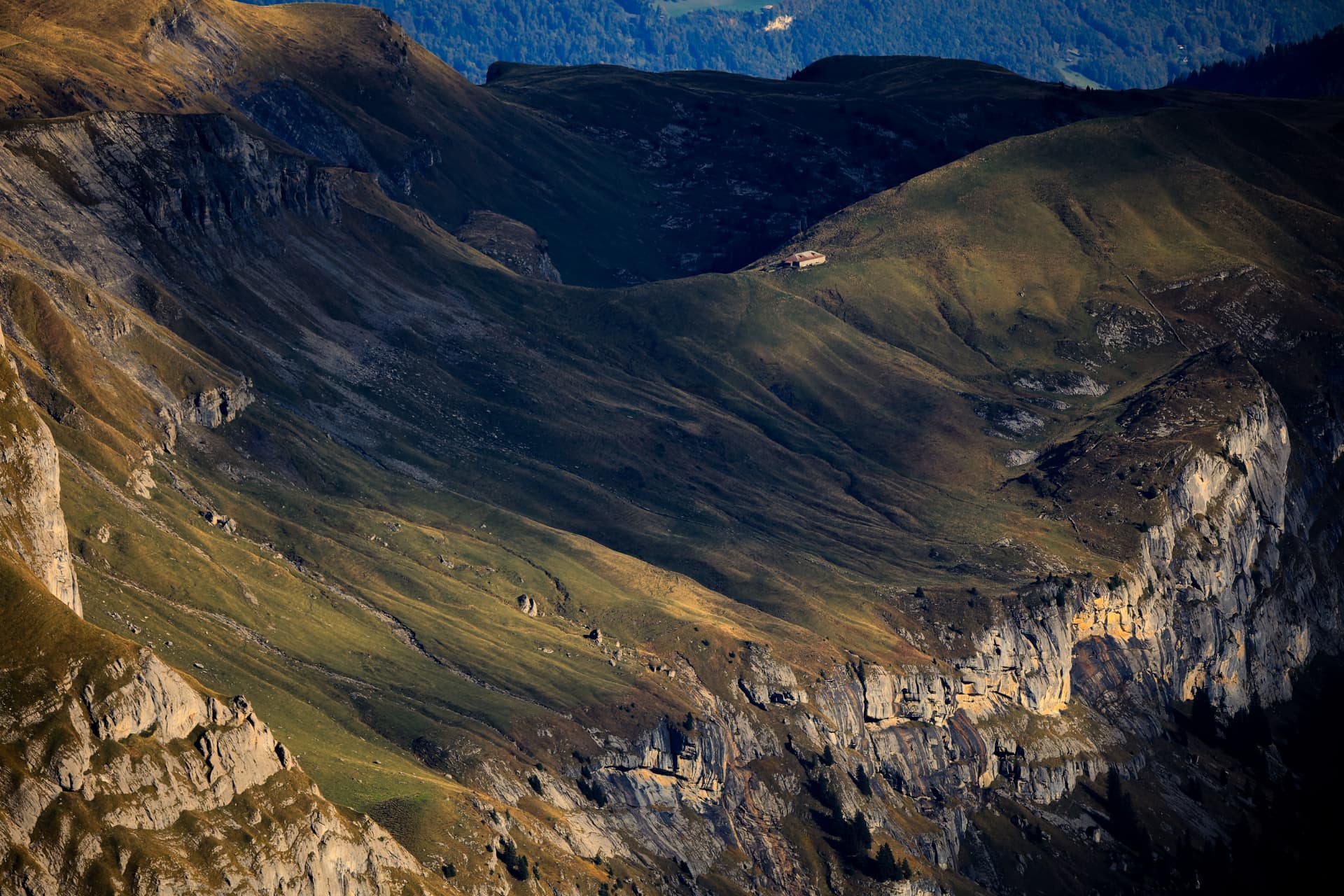 Einsame Alphütte auf grüner Weide zwischen Felswänden im Abendlicht