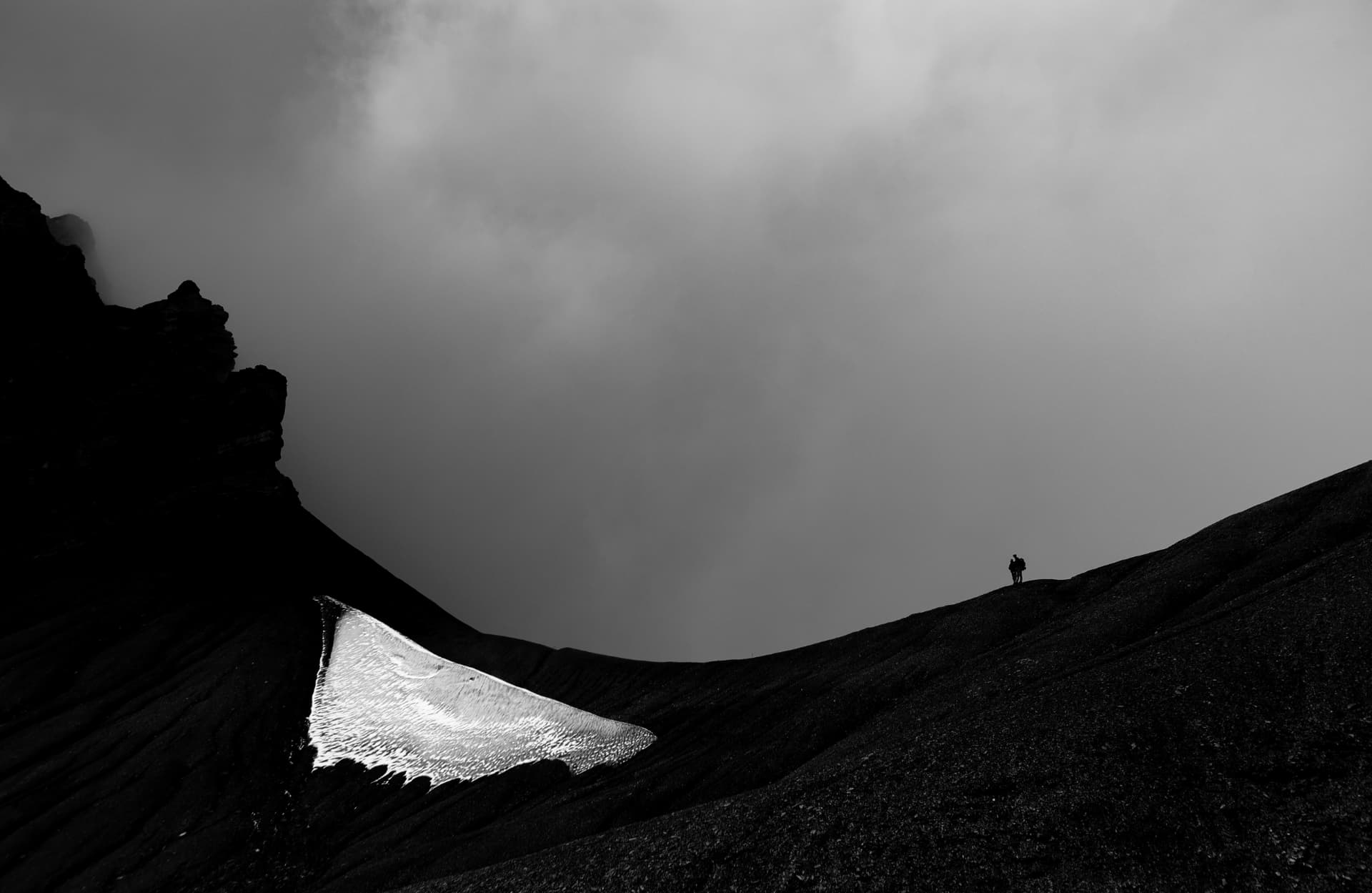 Schneefeld und Silhouette eines Wanderers auf dunklem Geröll, Dents du Midi