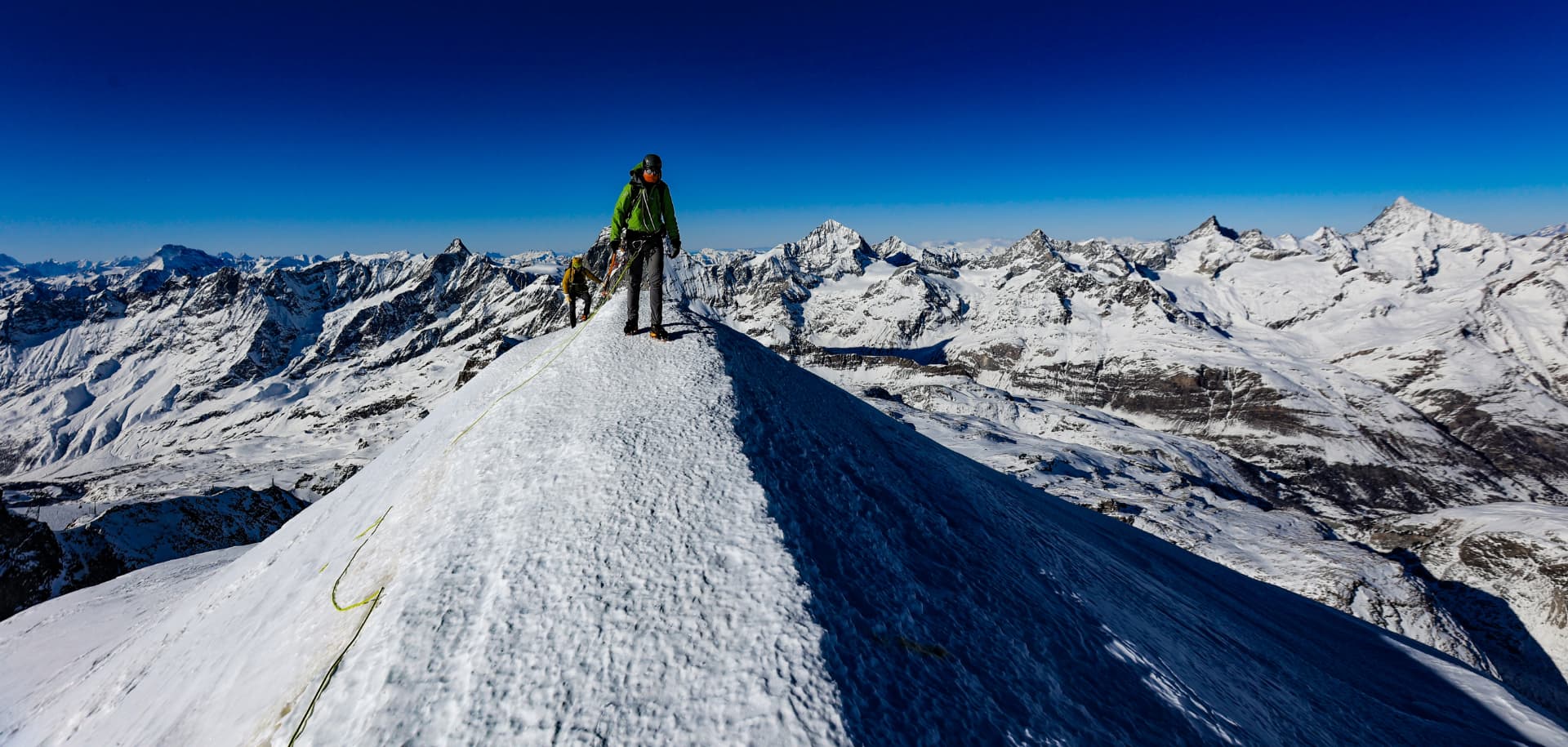 Bergsteiger auf dem schmalen Gipfelgrat des Breithorns mit Viertausender-Panorama