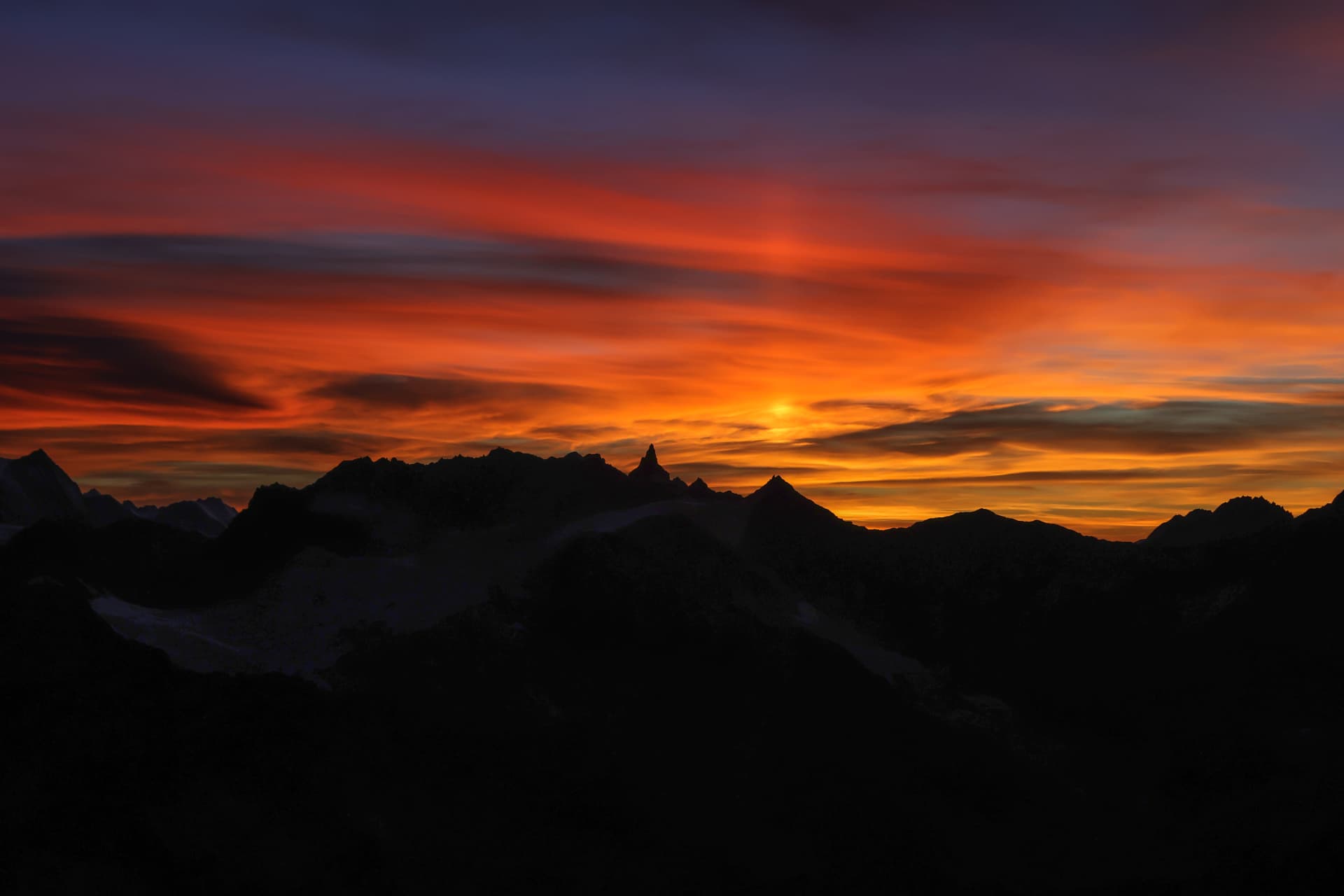 Sonnenuntergang über schwarzen Gratsilhouetten, der Himmel in Flammen