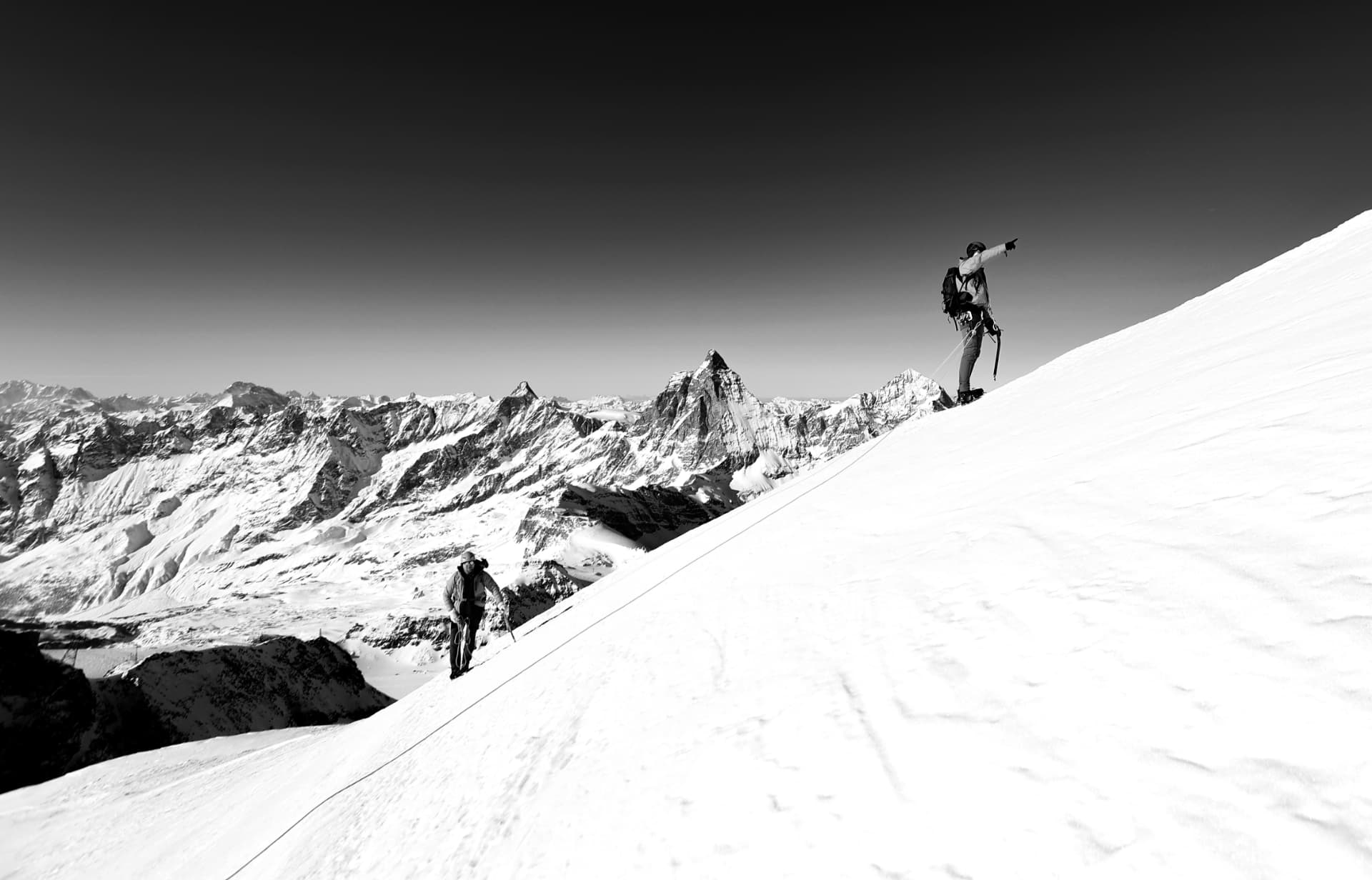 Zwei angeseilte Bergsteiger am Schneehang, dahinter das Matterhorn, schwarzweiss