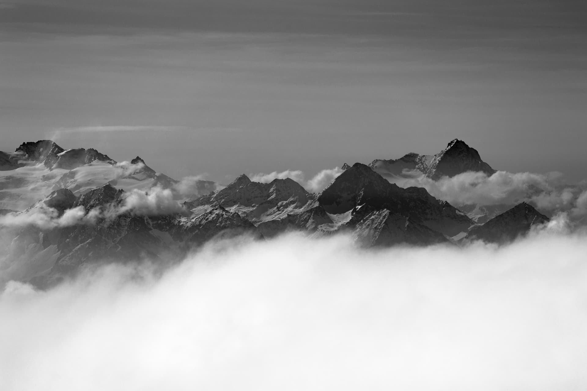 Weites Schwarzweisspanorama alpiner Gipfel über einem Wolkenmeer