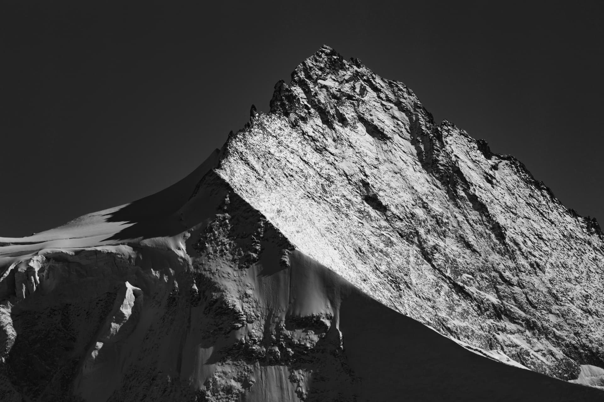 Verschneite Felswand und Eisformen in Schwarz-Weiß unter dunklem Himmel