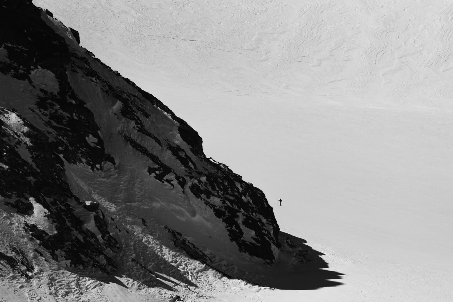 Einzelner Skitourengänger auf weitem Schneehang, schwarzweiss