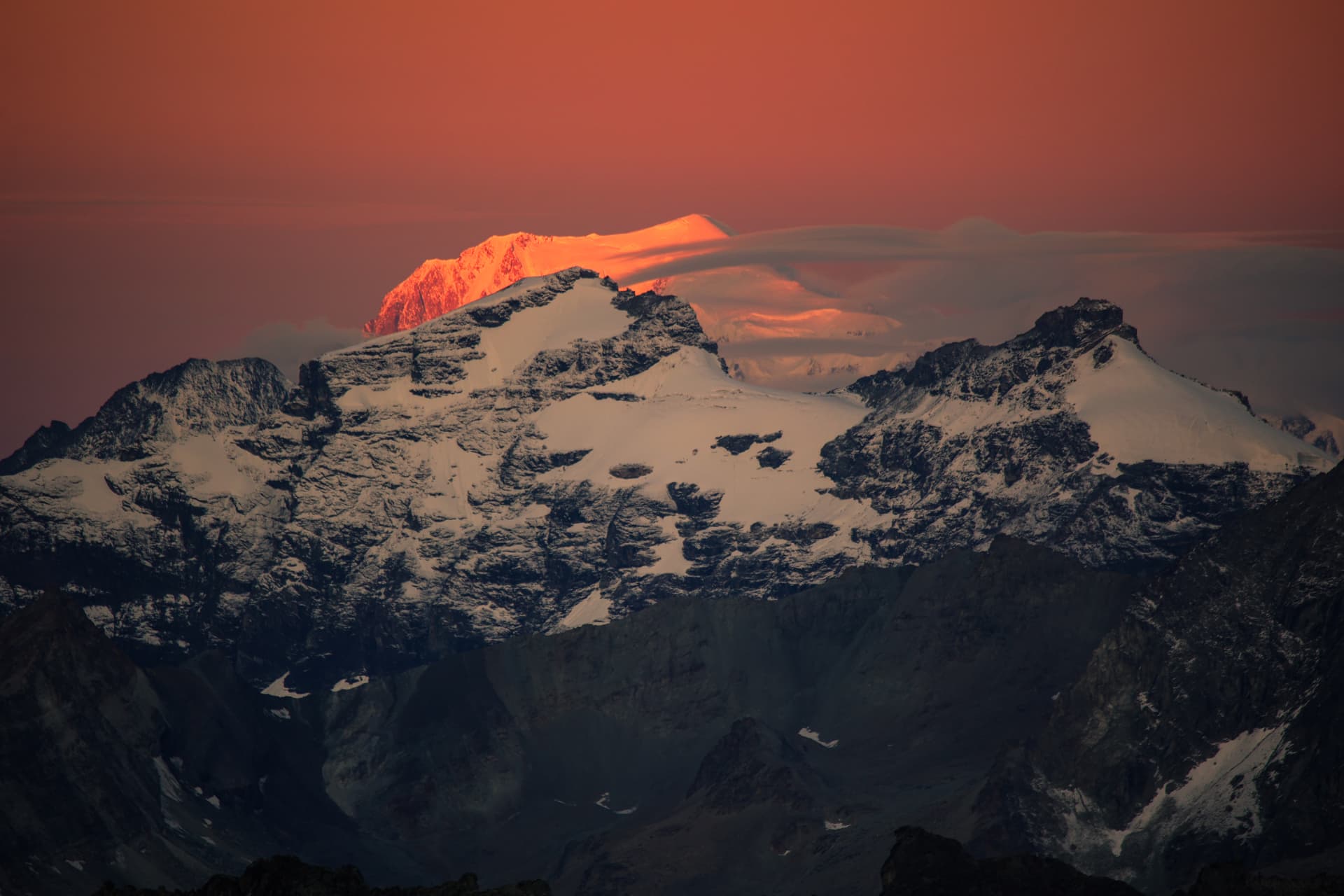 Sonnenaufgang über verschneitem Gipfel bei rotem Himmel