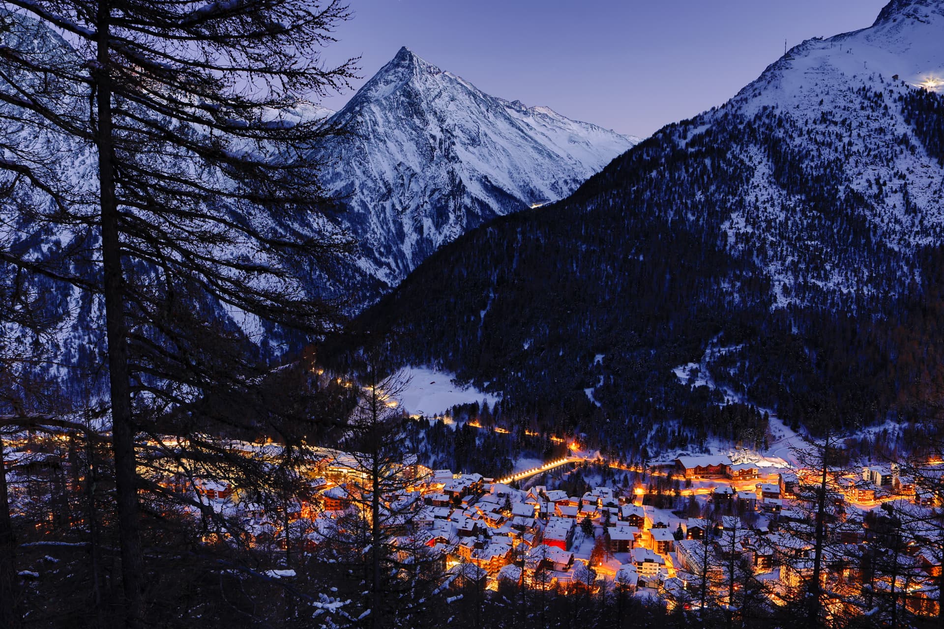 Die Lichter von Saas-Fee zur blauen Stunde mit verschneitem Gipfel
