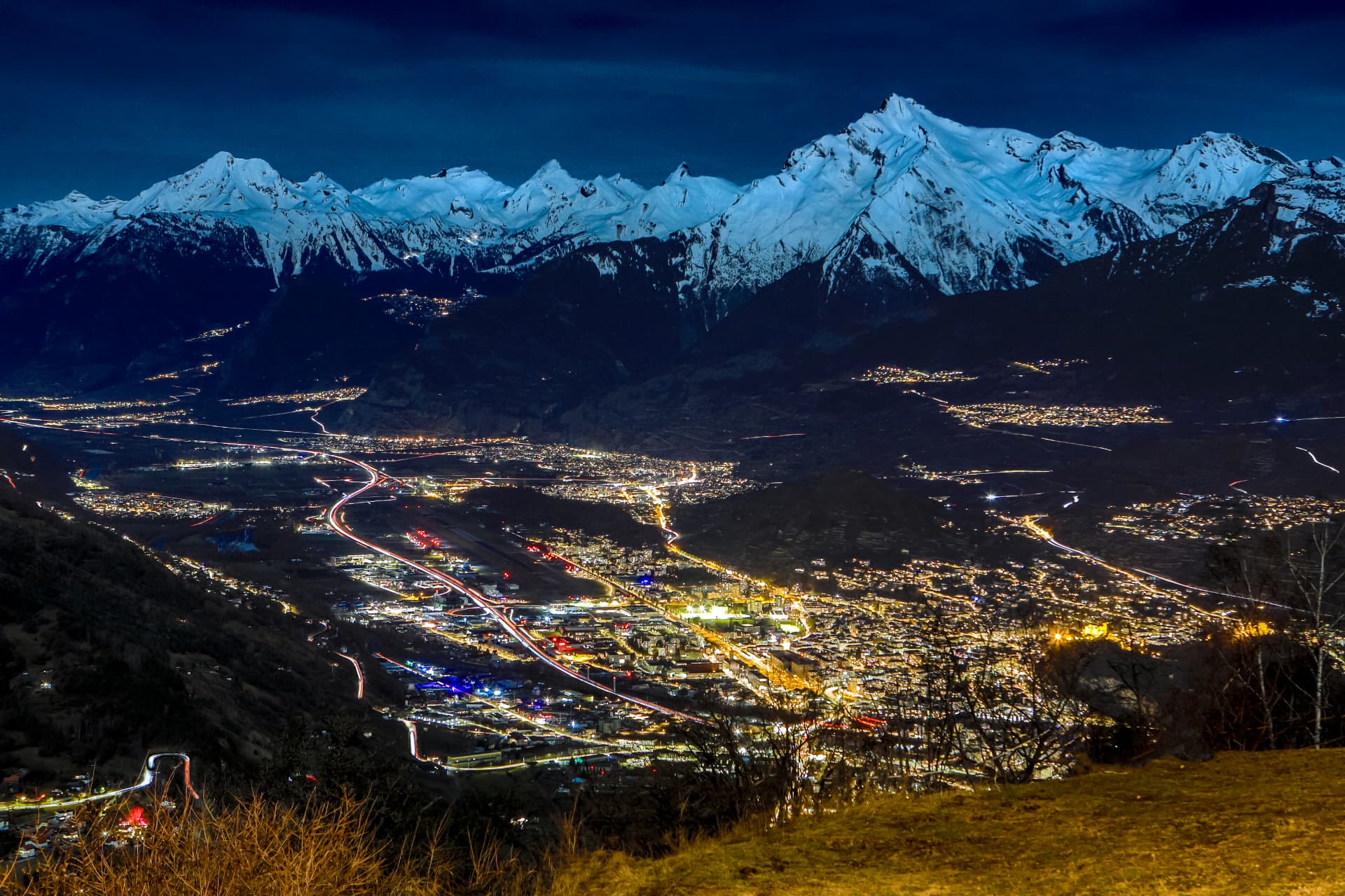 Nachtblick auf die Lichter von Sion und das Rhonetal unter den verschneiten Berner Alpen