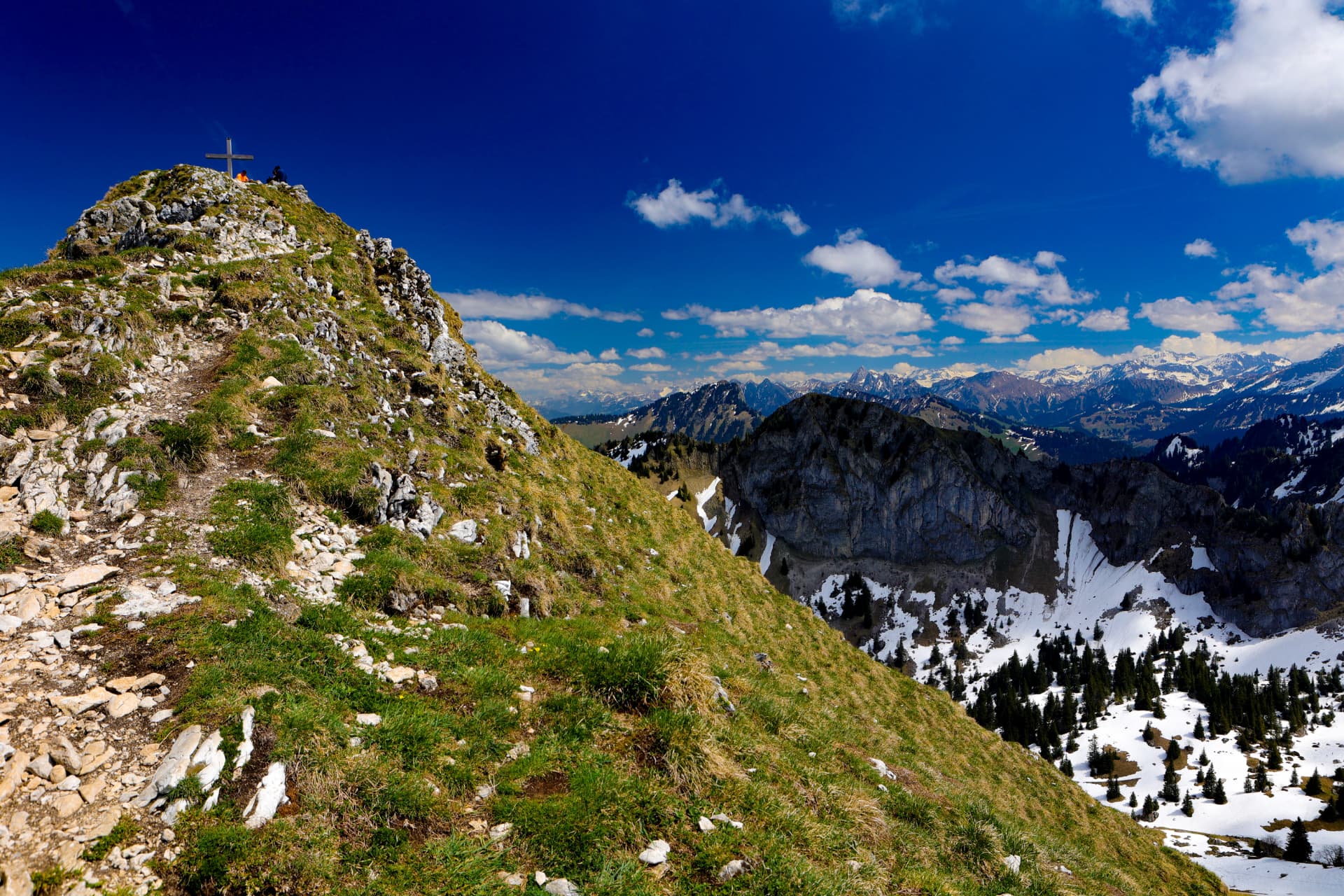 Grasgrat mit dem Gipfelkreuz der Dent de Jaman und Felswänden im Hintergrund
