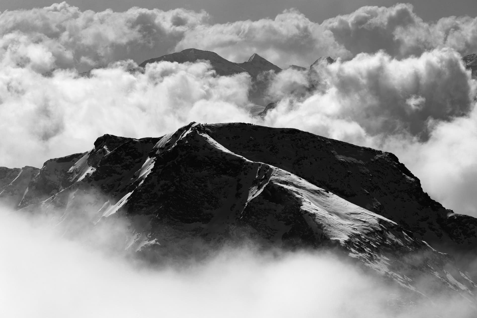 Verschneiter Grat zwischen dichten Wolken in Schwarzweiss