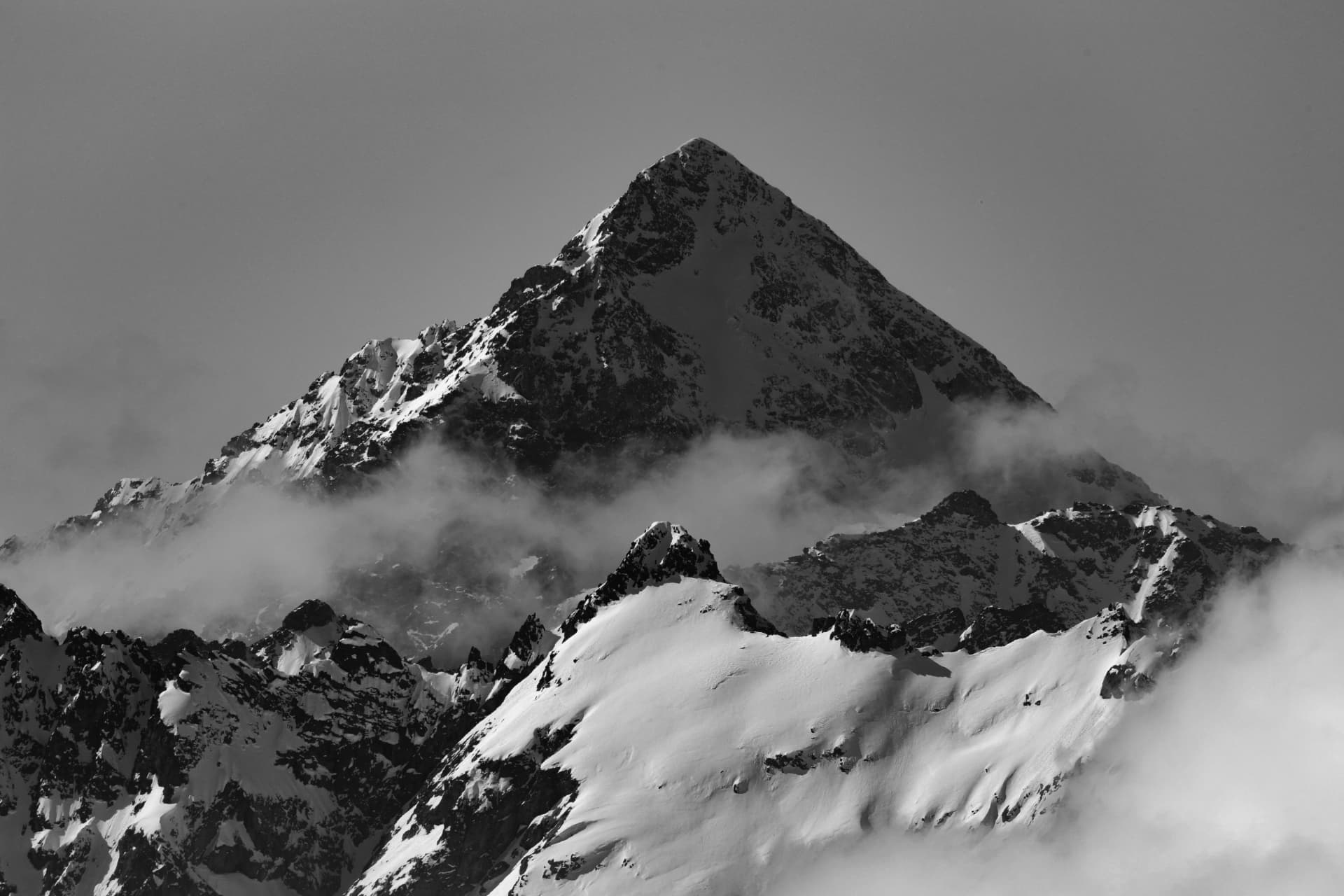 Schwarzweisse Pyramide eines verschneiten Gipfels mit Wolken am Fuss