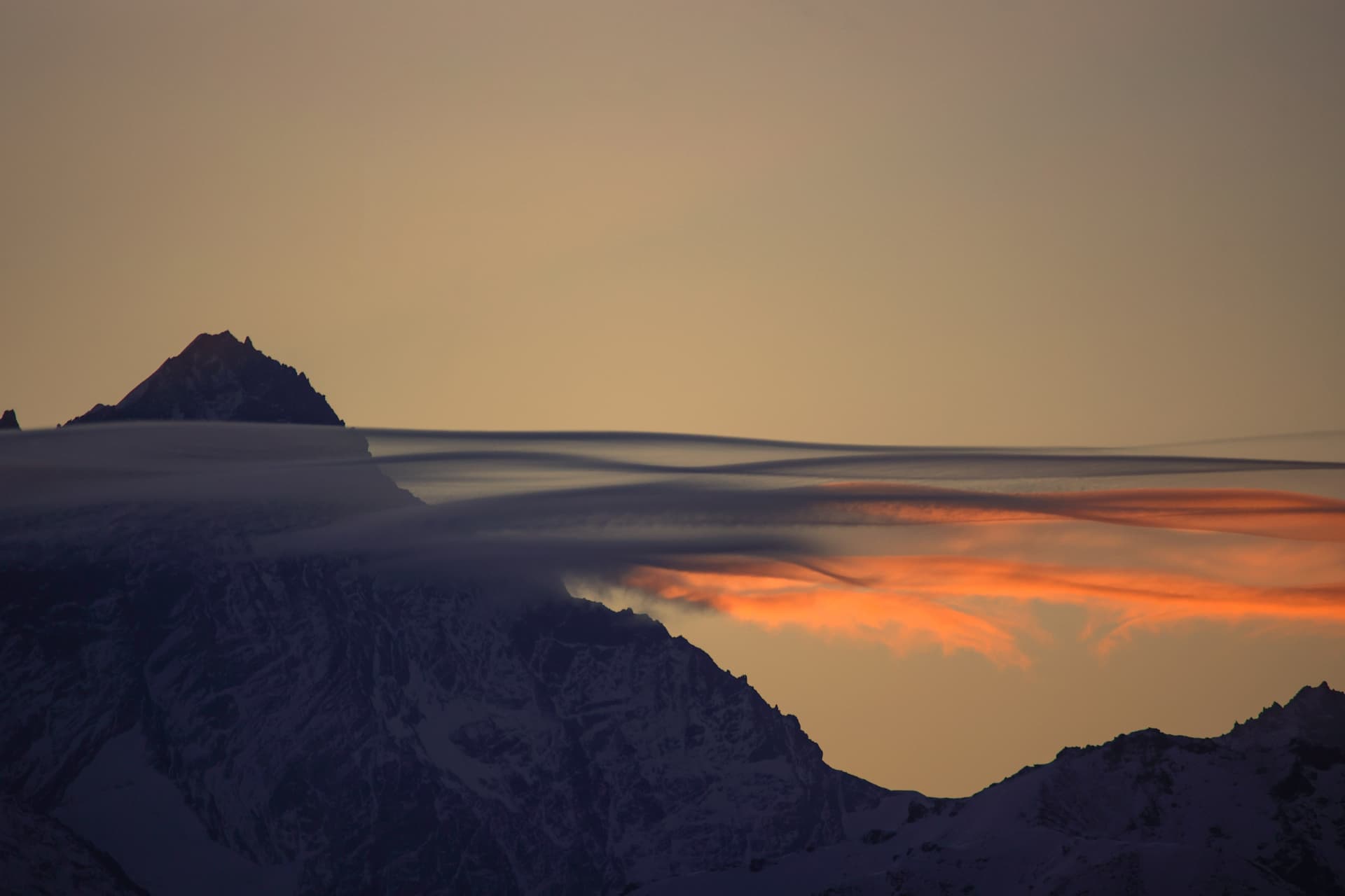 Lenticularis-Wolken über einem verschneiten Gipfel im orangen Licht