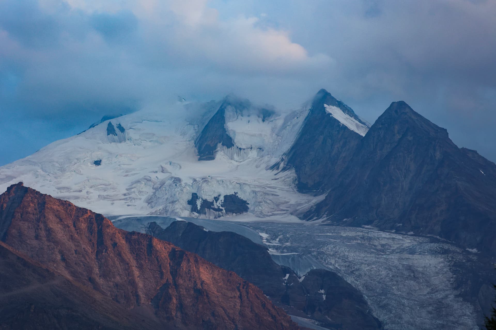 Gletscher und verschneite Gipfel im kühlen Dämmerlicht, rote Felswand im Vordergrund