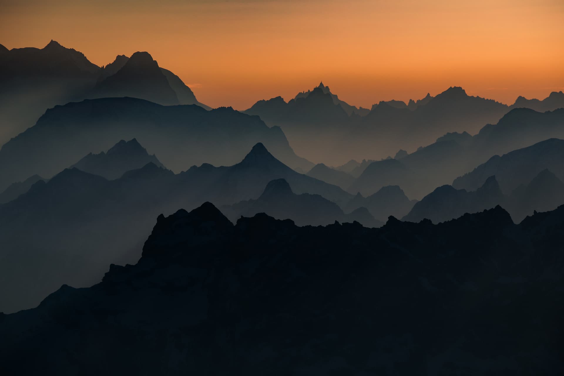 Gestaffelte Bergkämme im orangen Dunst bei Sonnenaufgang, gesehen von 4000 Metern