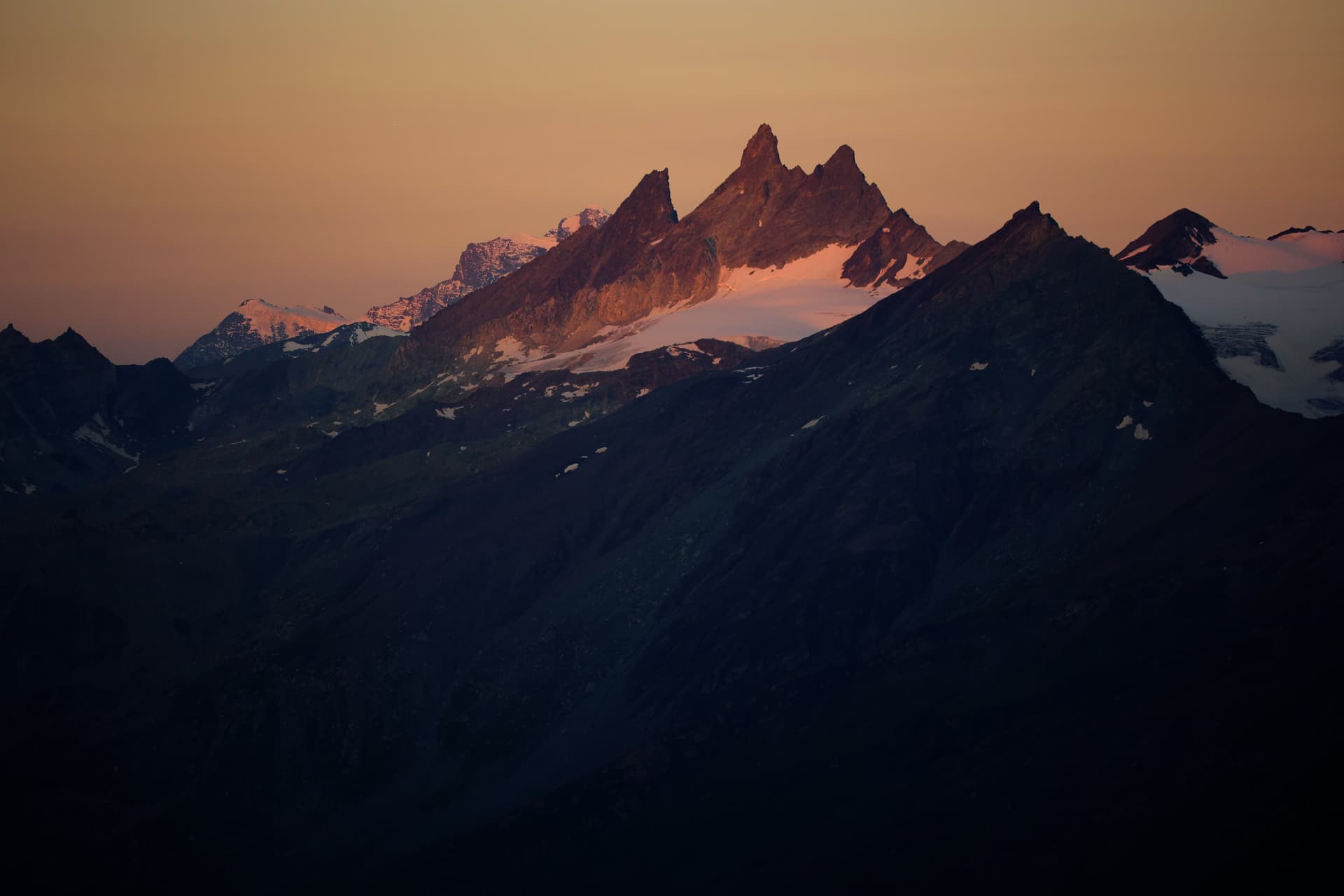 Felsgipfel im roten Licht des Sonnenaufgangs über dunklen Flanken