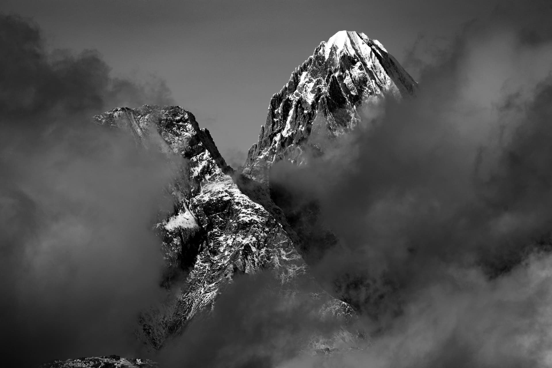 Schwarzweisser verschneiter Gipfel, auftauchend aus dunklen Wolken