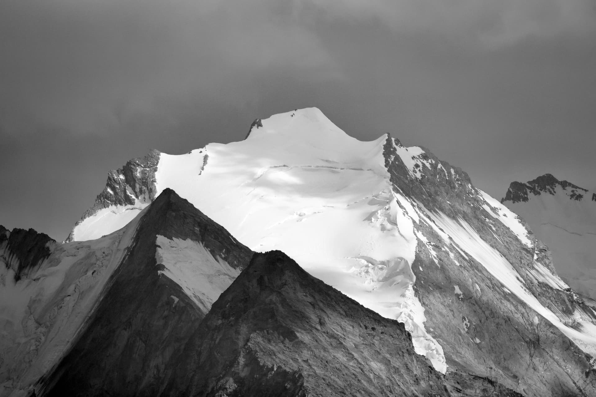 Schwarzweiss-Foto der Schneekuppe des Bishorns über dunklen Graten