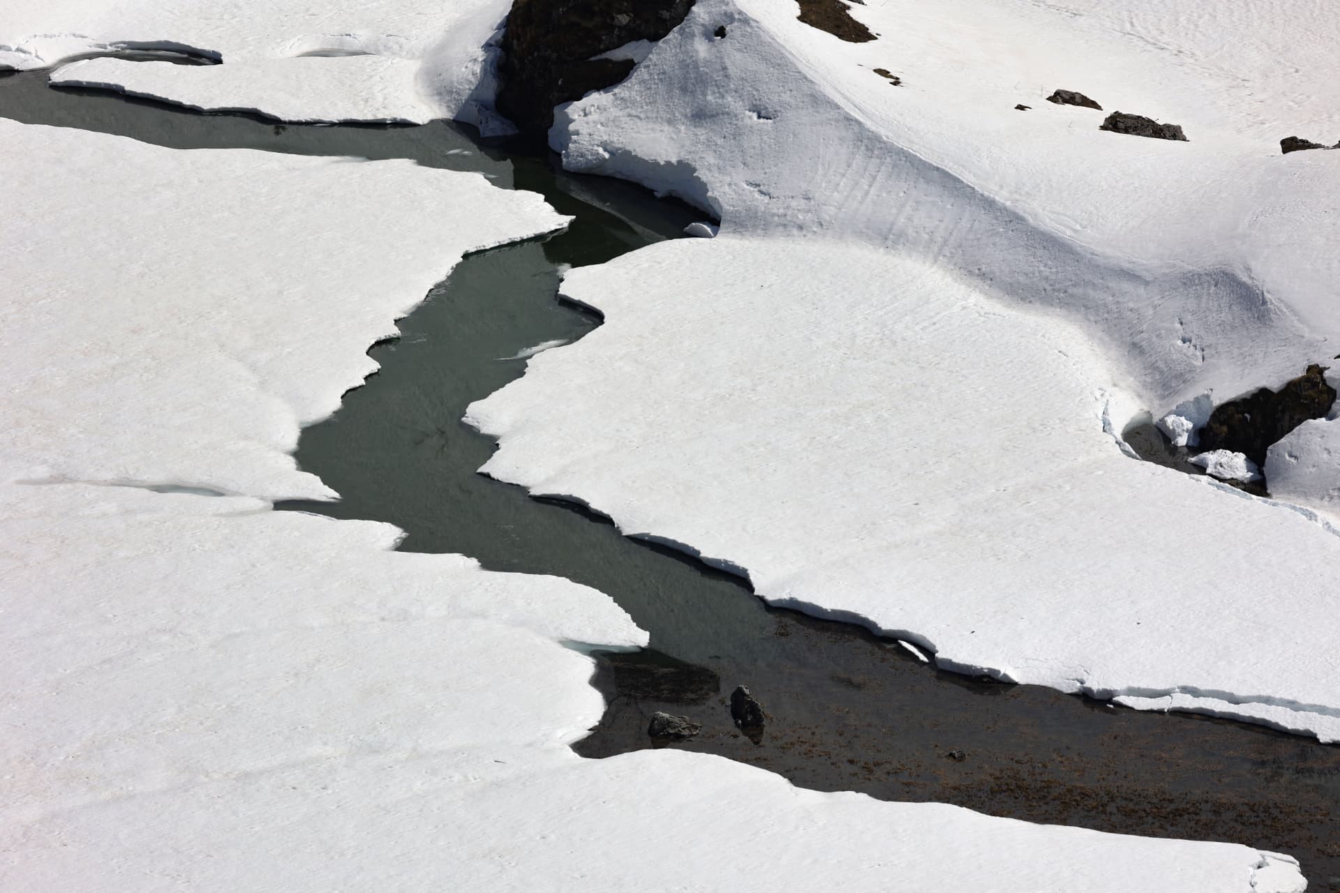 Dunkle Schmelzwasserrinne zwischen Schneefeldern