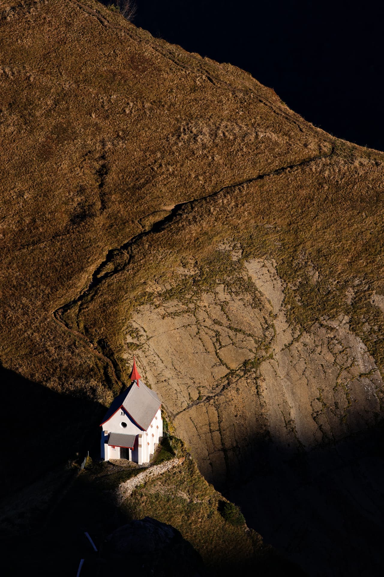 Weiße Kapelle mit rotem Dach an einem steilen goldgelben Hang