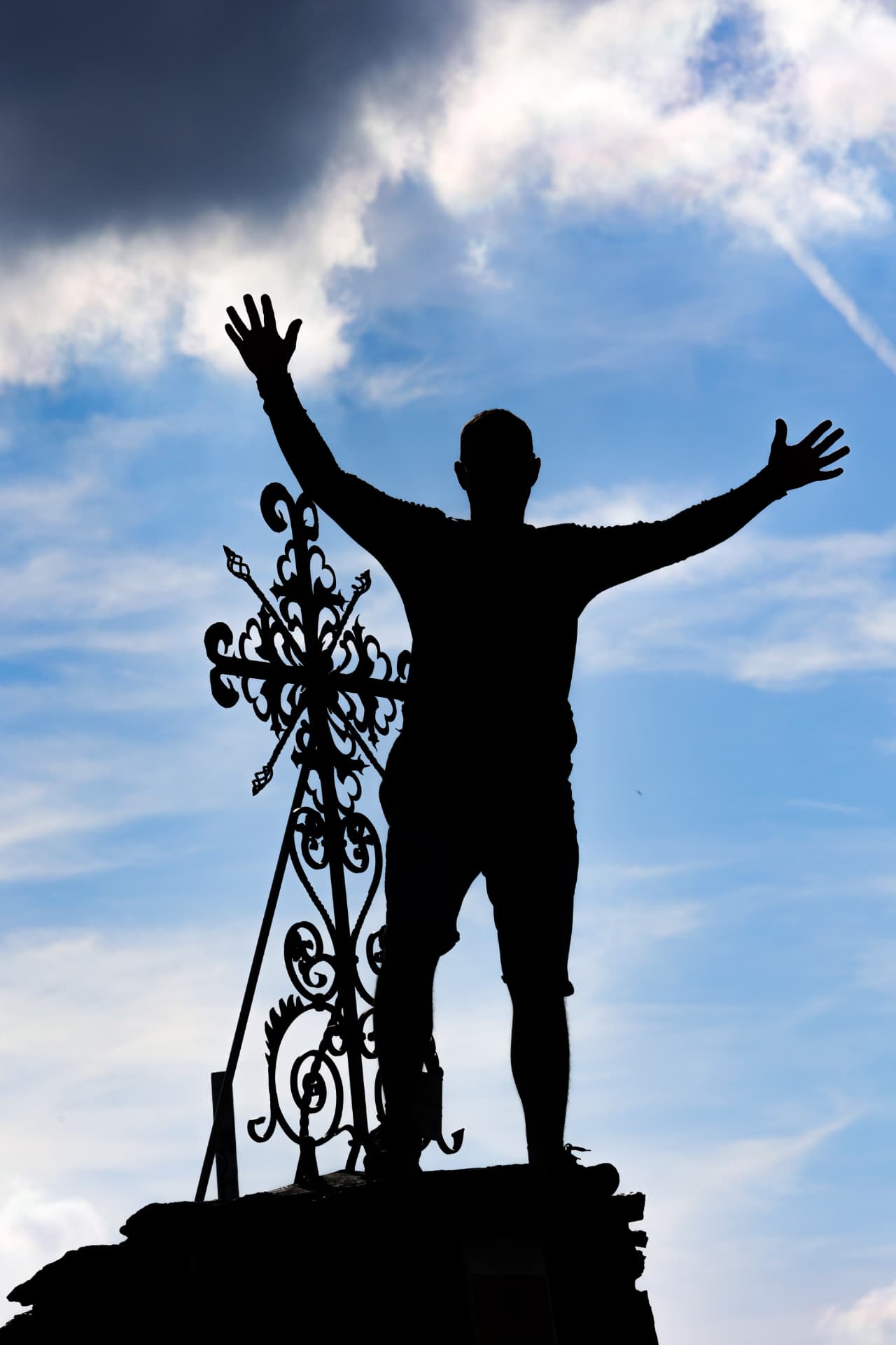 Silhouette mit erhobenen Armen am geschmiedeten Gipfelkreuz des Augstbordhorns