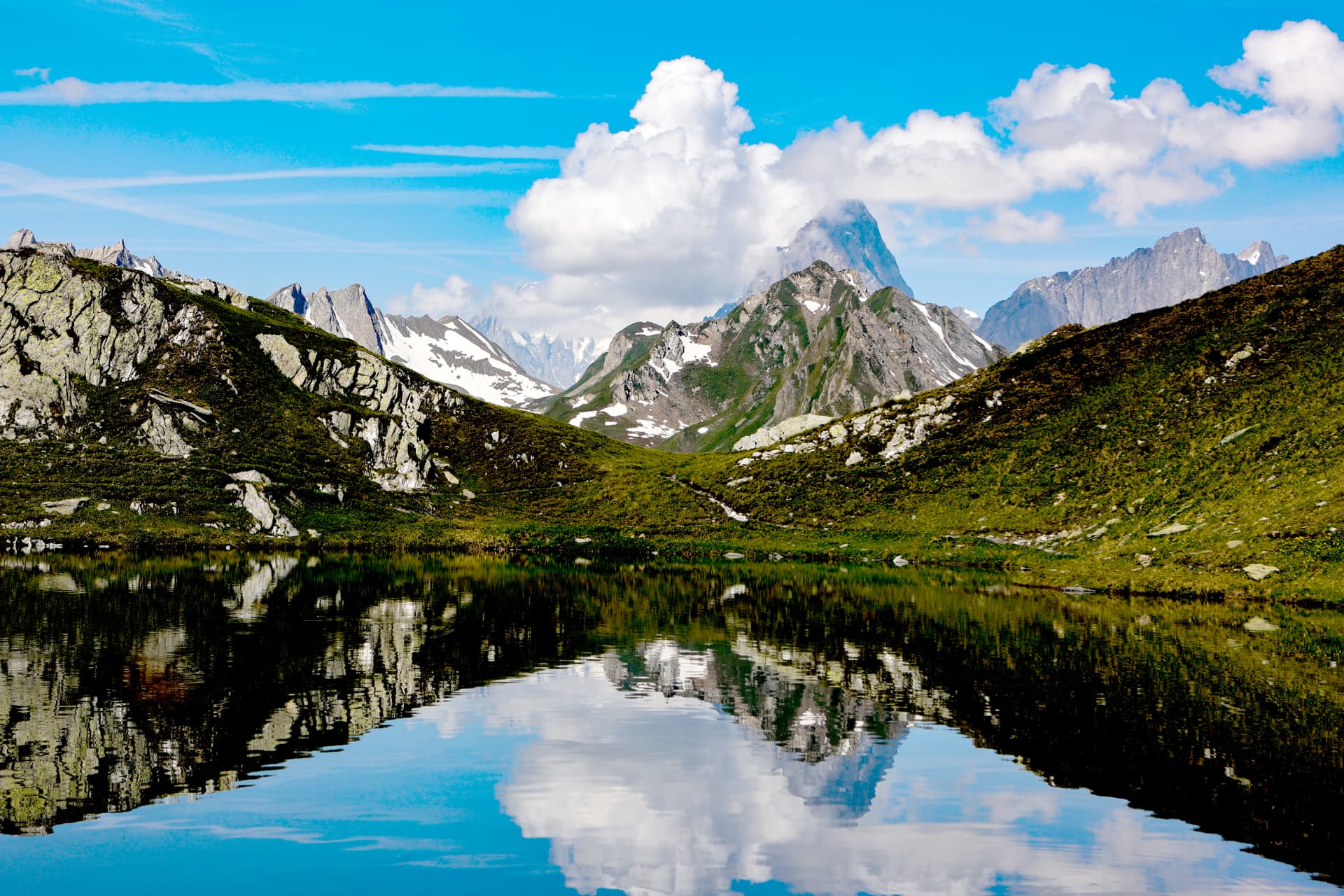 Felsgrate und Wolken spiegeln sich in einem Alpensee