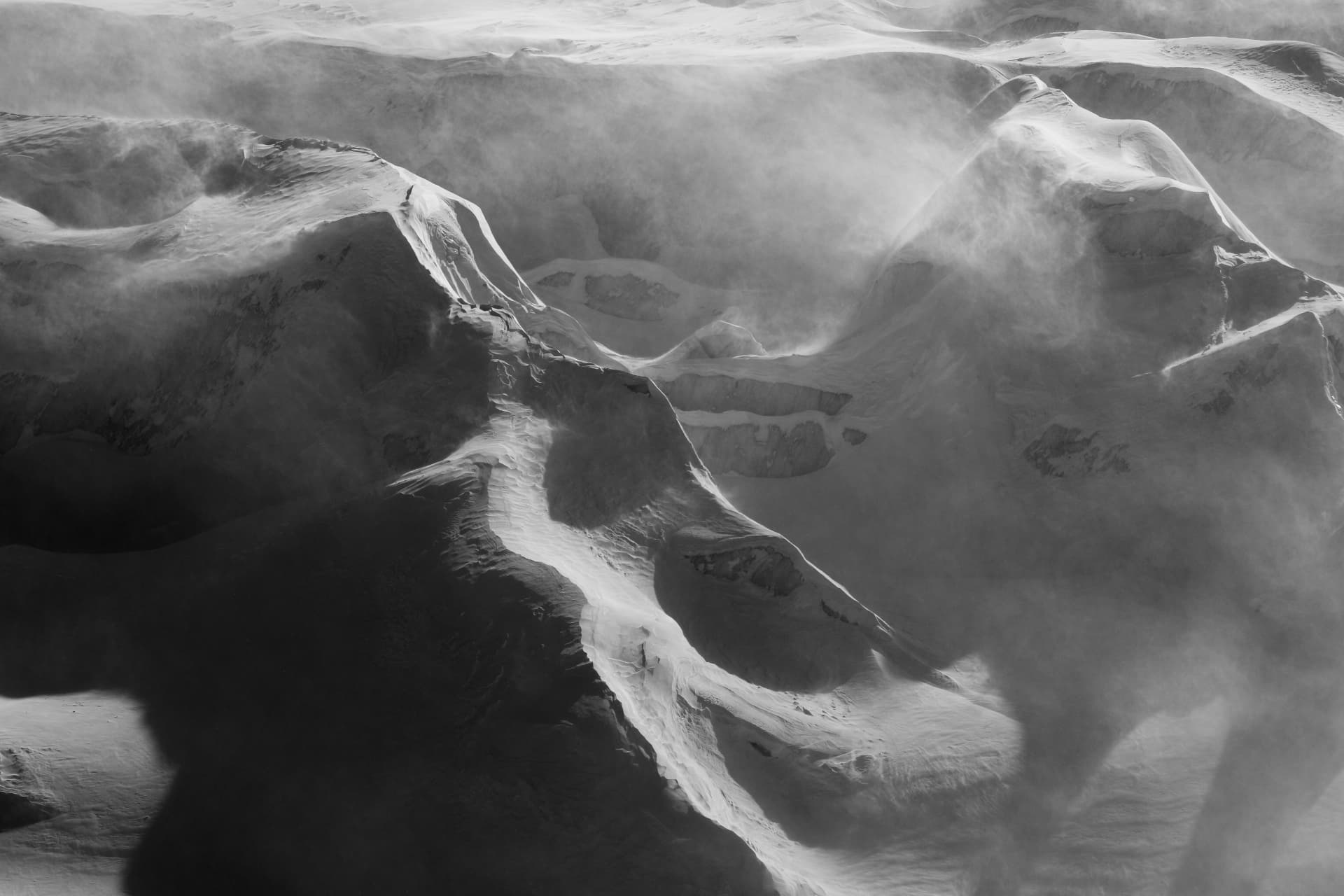 Schwarzweißes Bild von Schneetreiben auf Gletscher und Graten