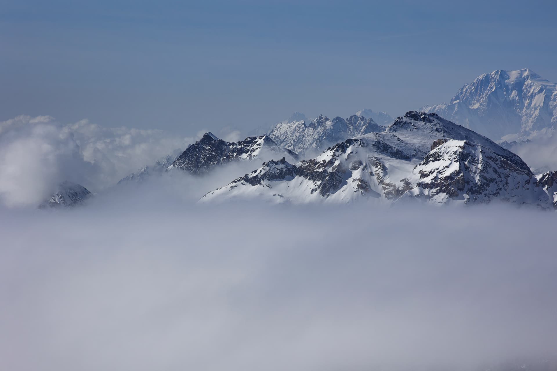 Verschneite Bergkämme über Wolken unter blauem Himmel
