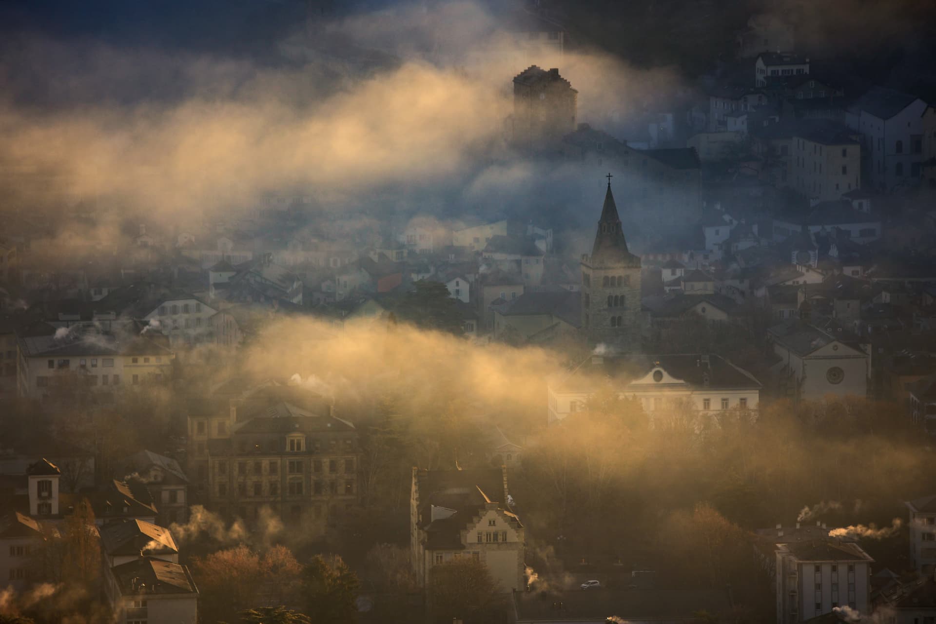 Altstadt von Sion im Morgennebel mit Kathedralturm und Kaminrauch