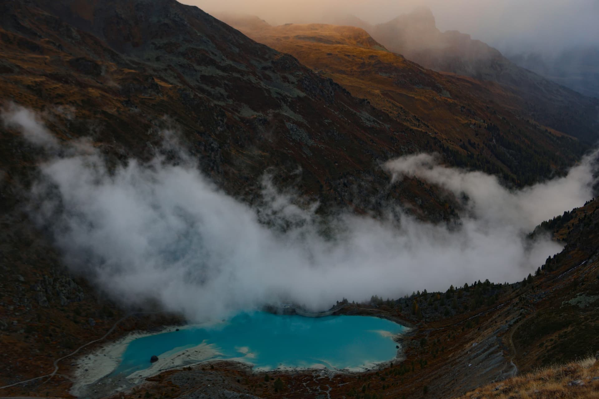 Türkisfarbener Alpensee unter Nebelschwaden und herbstlichen Hängen