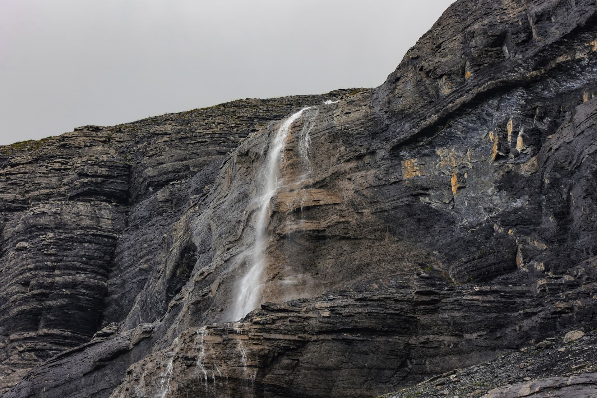 Wasserfall über der dunklen Felswand am Oeschinensee