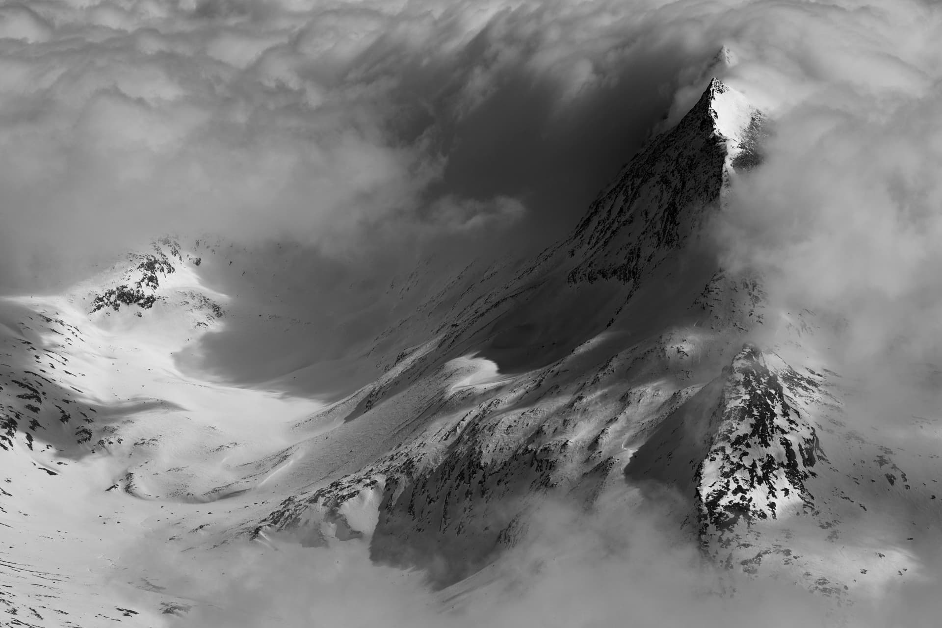 Licht und Schatten an einem verschneiten Gipfel in wirbelnden Wolken, schwarzweiss