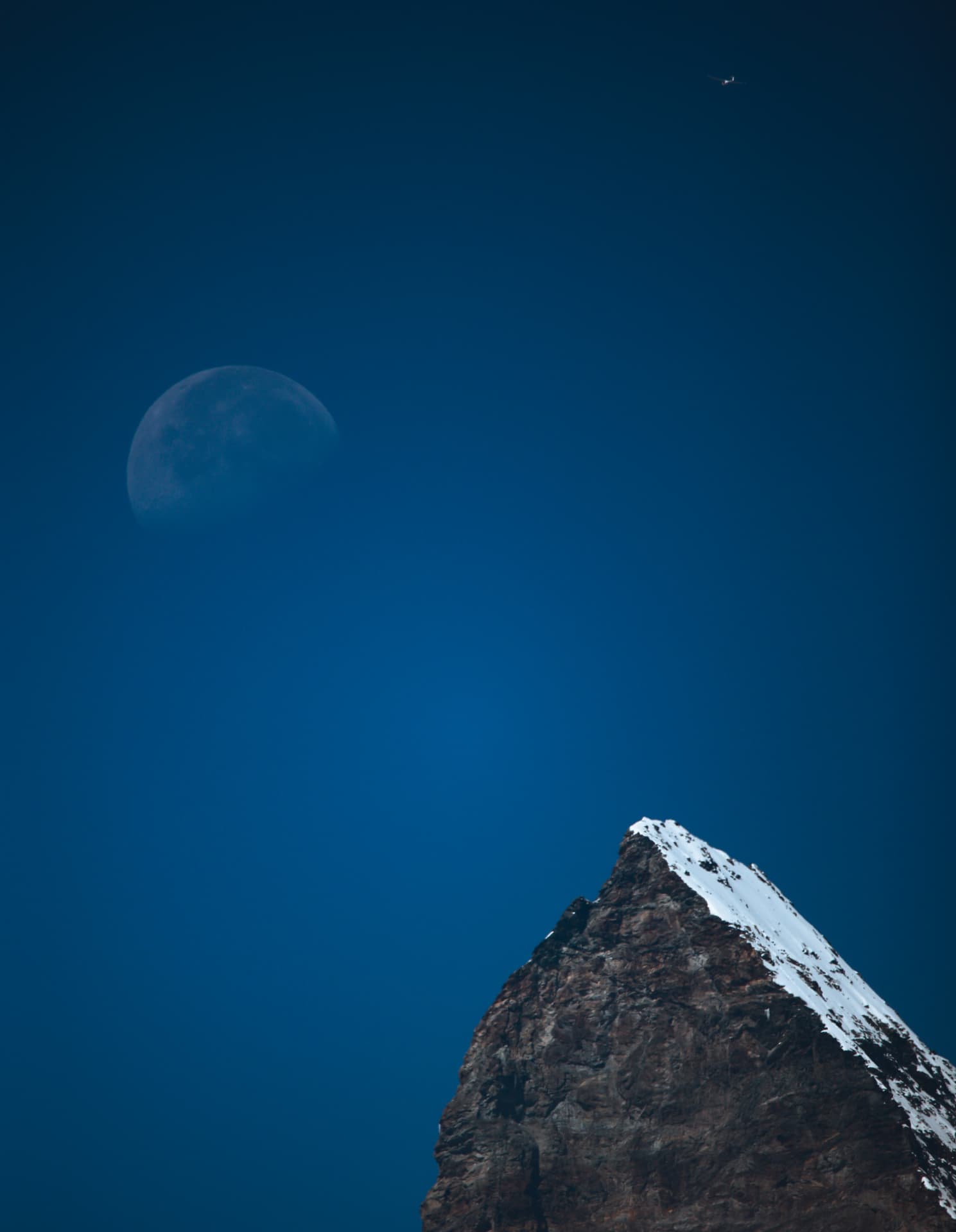 Mond über einem verschneiten Gipfel im dunkelblauen Himmel