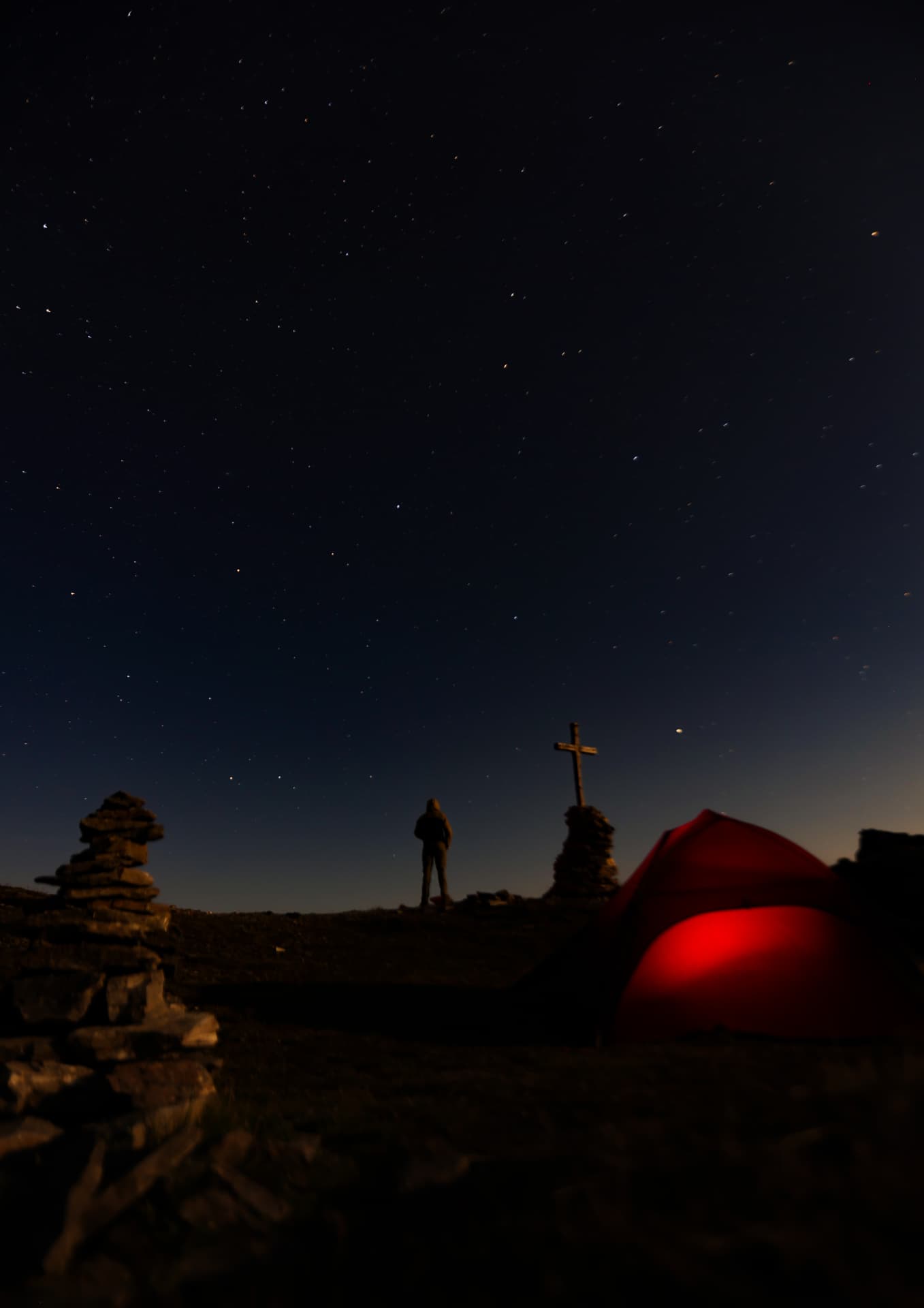 Rotes Zelt und Gipfelkreuz auf dem Pass unter Sternenhimmel