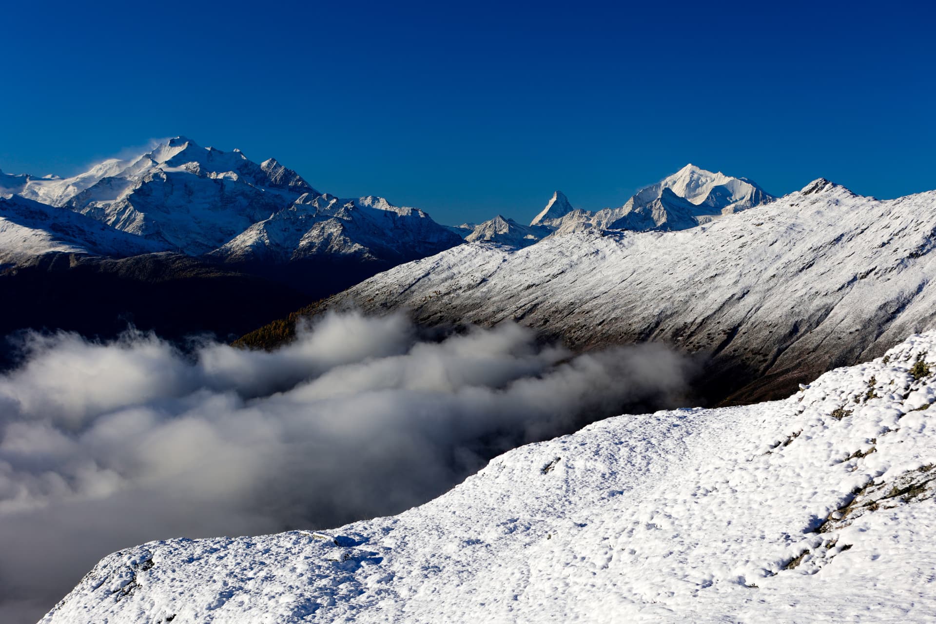 Nebelmeer unter einem verschneiten Grat und ferne Walliser Gipfel
