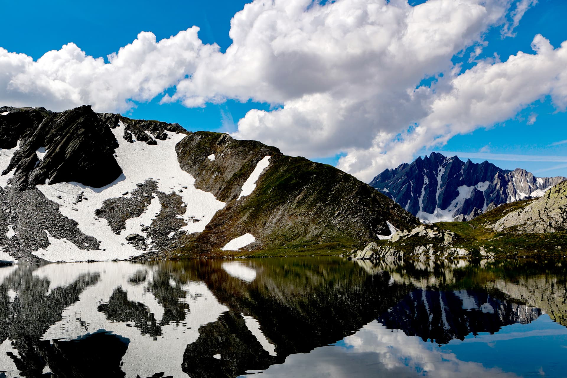 Schneereste am Seeufer vor felsigen Bergpanoramen