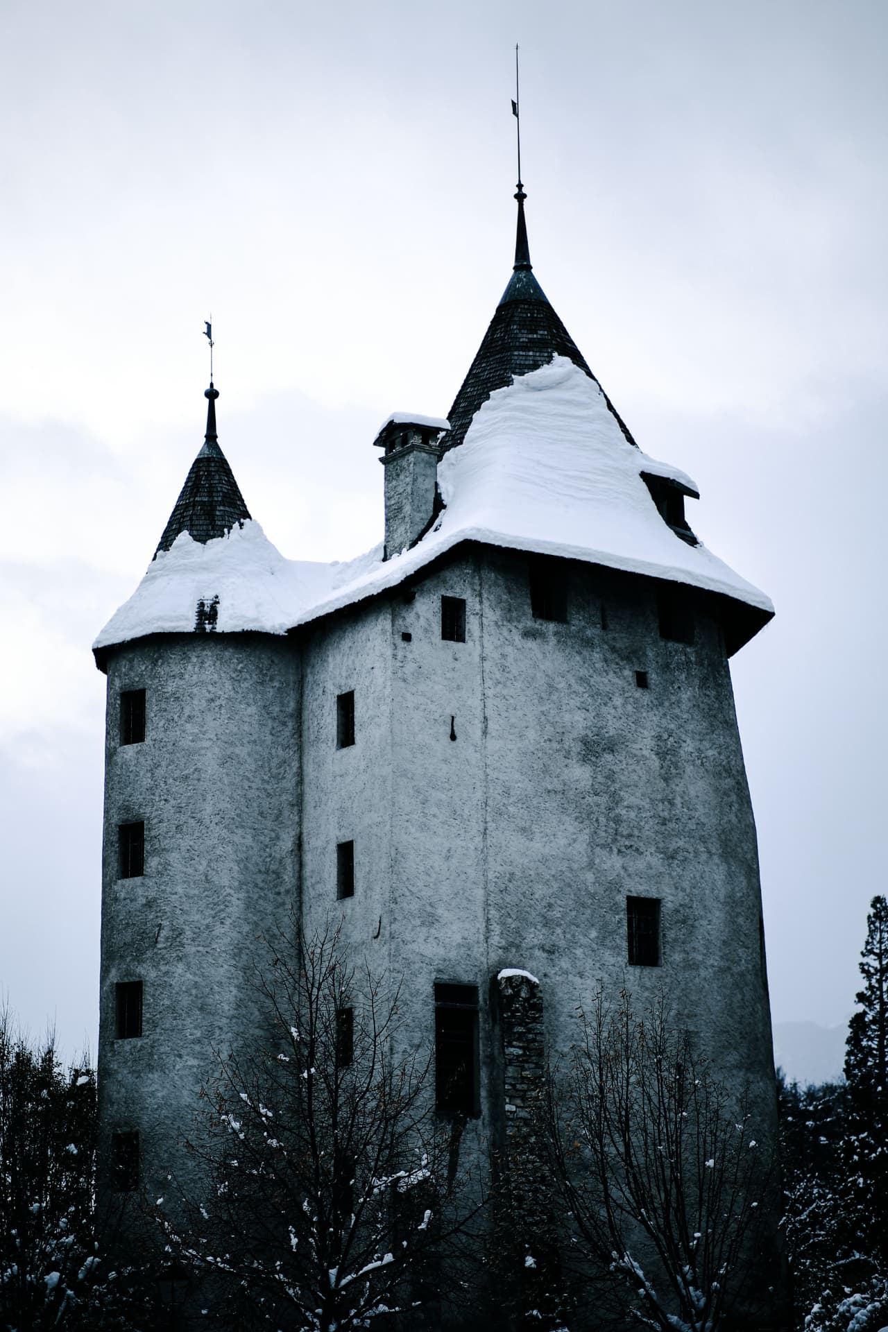Verschneiter Burgturm mit zwei spitzen Dächern in winterlicher Walliser Landschaft
