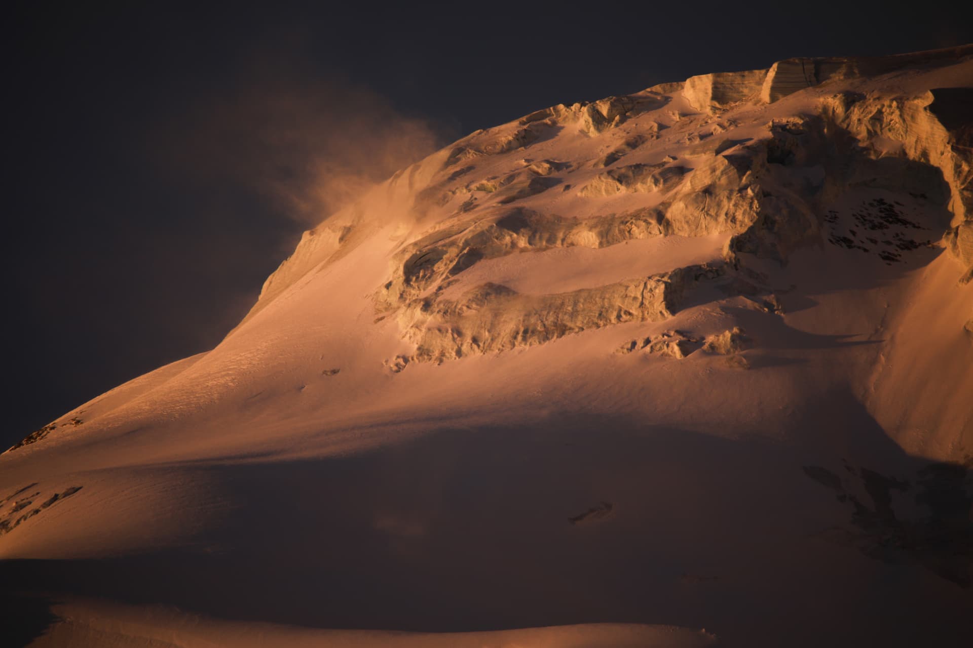 Schneekuppe im warmen Morgenlicht mit Schneefahne am Grat