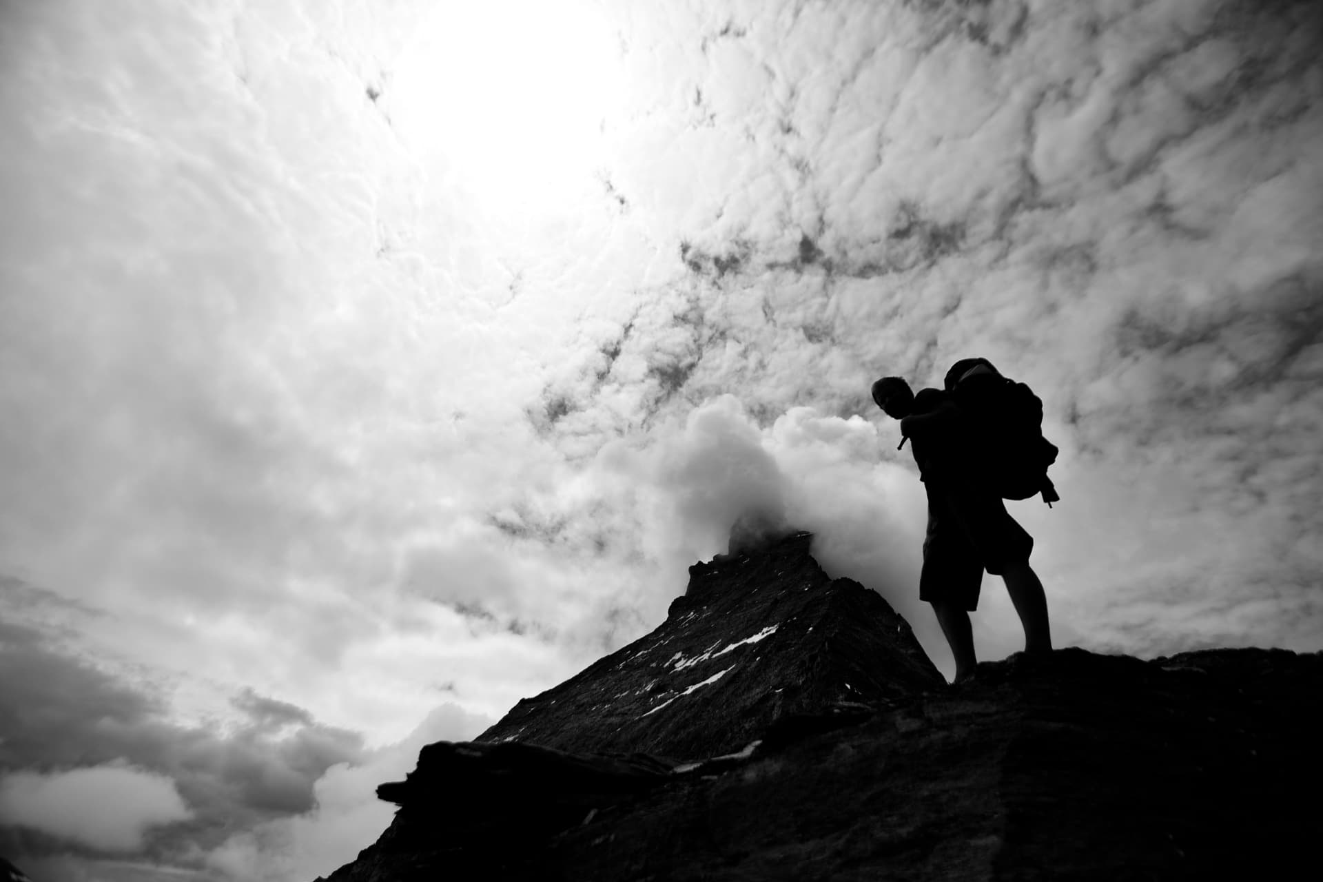 Schwarzweisse Silhouette eines Fotografen mit Rucksack auf dem Grat