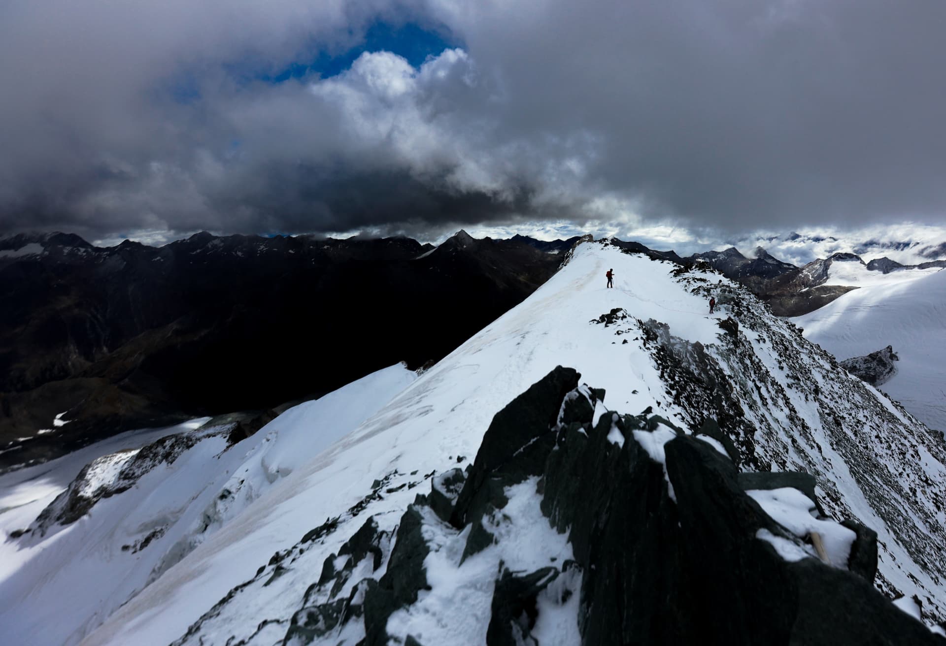 Gipfelgrat des Allalinhorns mit Bergsteiger und Gewitterwolken